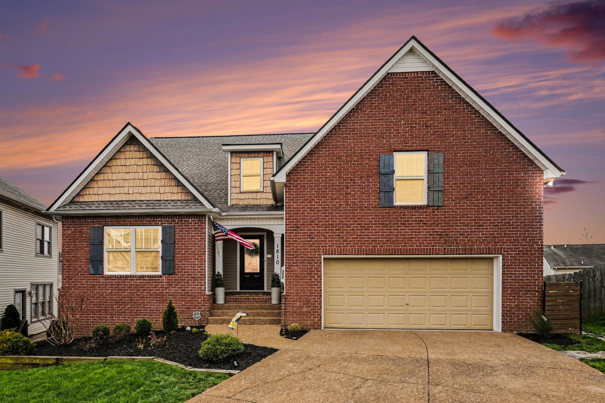 Two-story red brick house with a two-car garage and American flag at sunset.