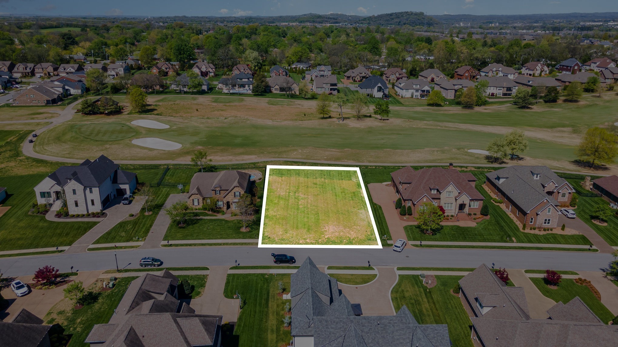 Vacant lot outlined in white between neighboring homes and a golf course.