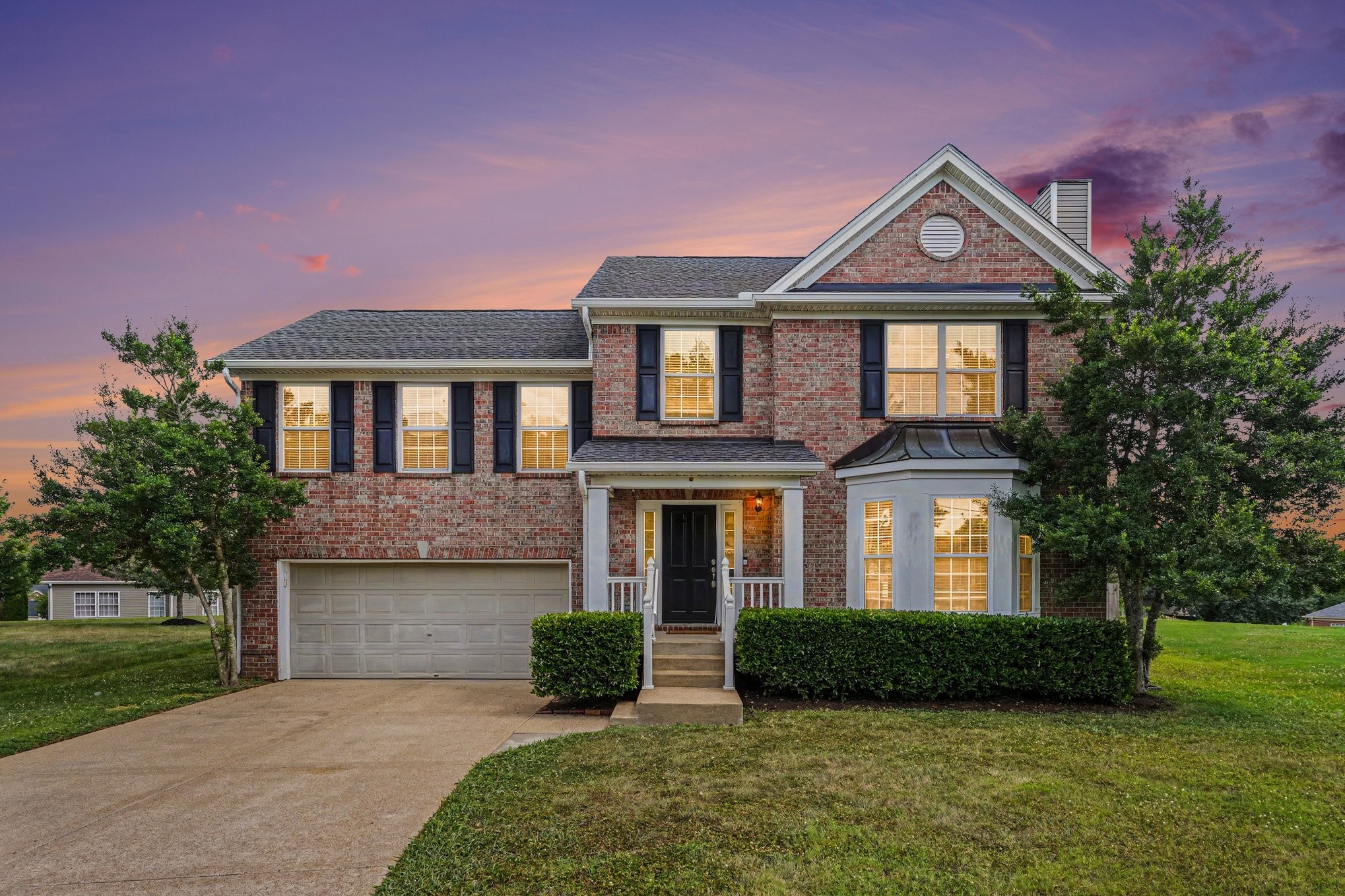 Two-story brick home with a two-car garage and glowing windows at dusk.