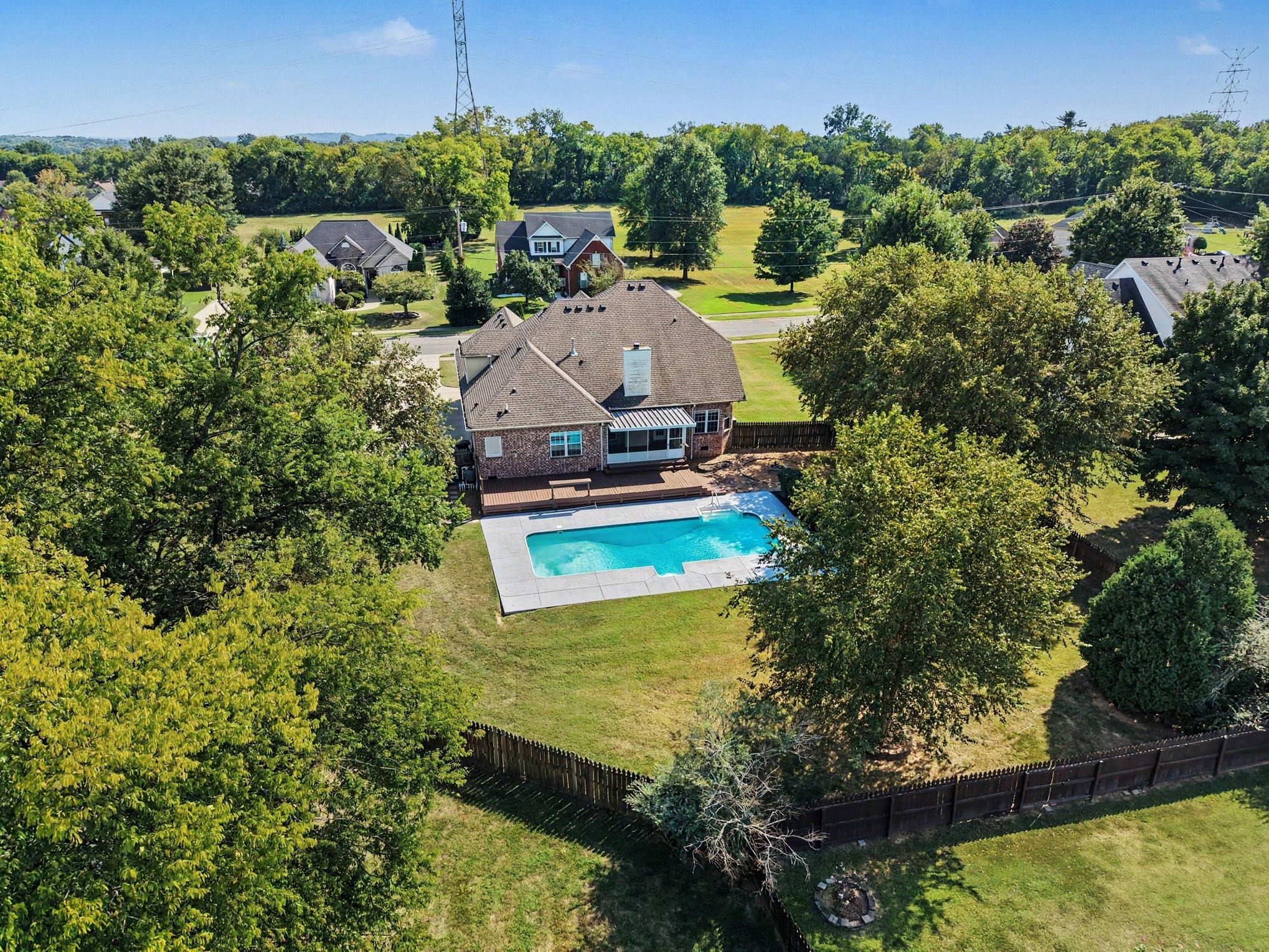 Aerial view of a brick home with a fenced backyard, deck, and swimming pool.