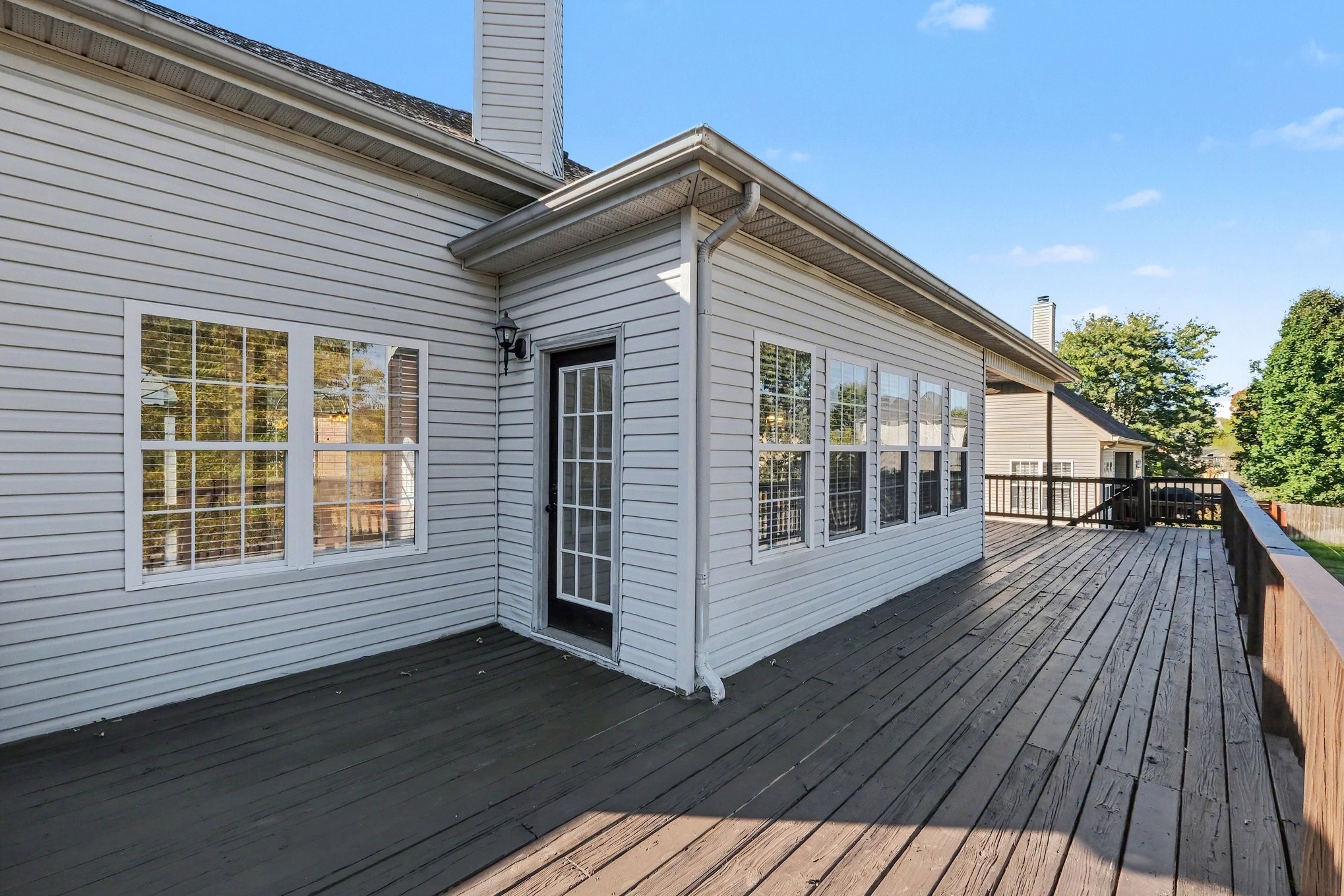 Rear deck along a light-gray home, with multiple windows and a glass-paneled door.