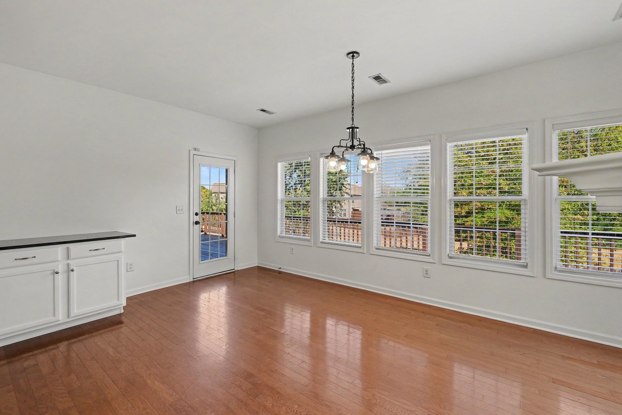 Empty dining area with hardwood floors, a chandelier, and a wall of windows.