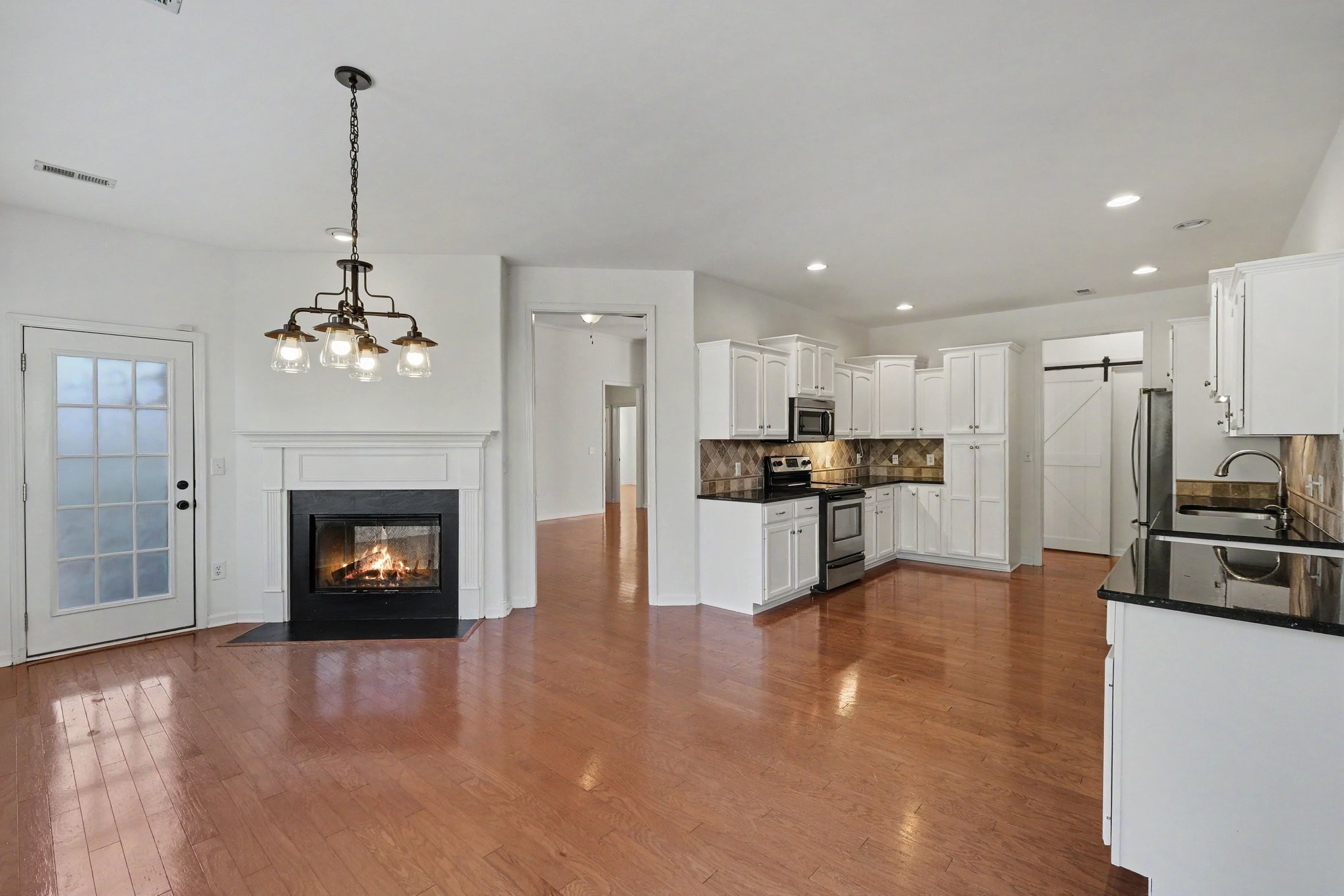 Kitchen and living area with white cabinets, hardwood floors, and a lit fireplace.