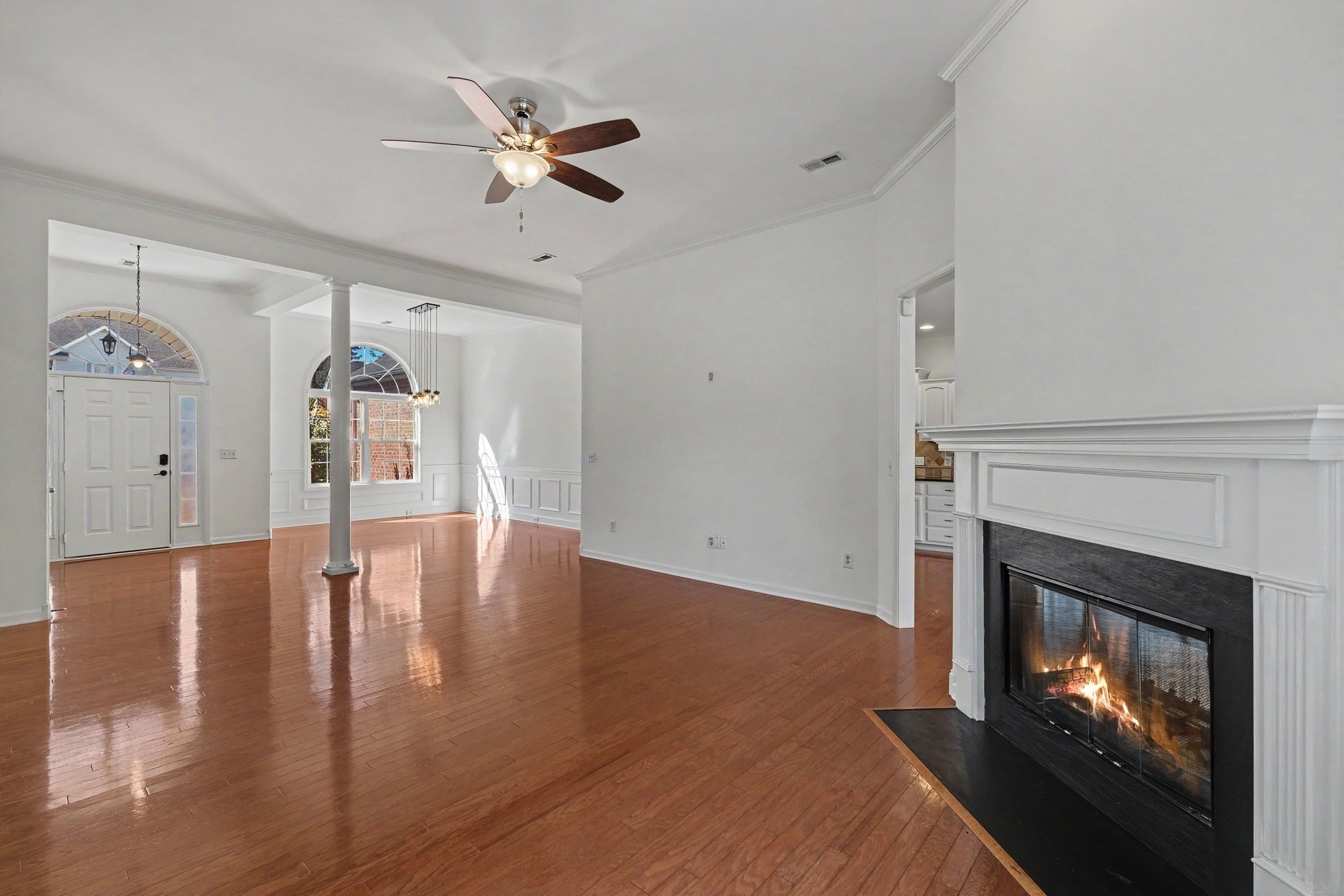 Vacant living room with polished hardwood floors and a lit fireplace.