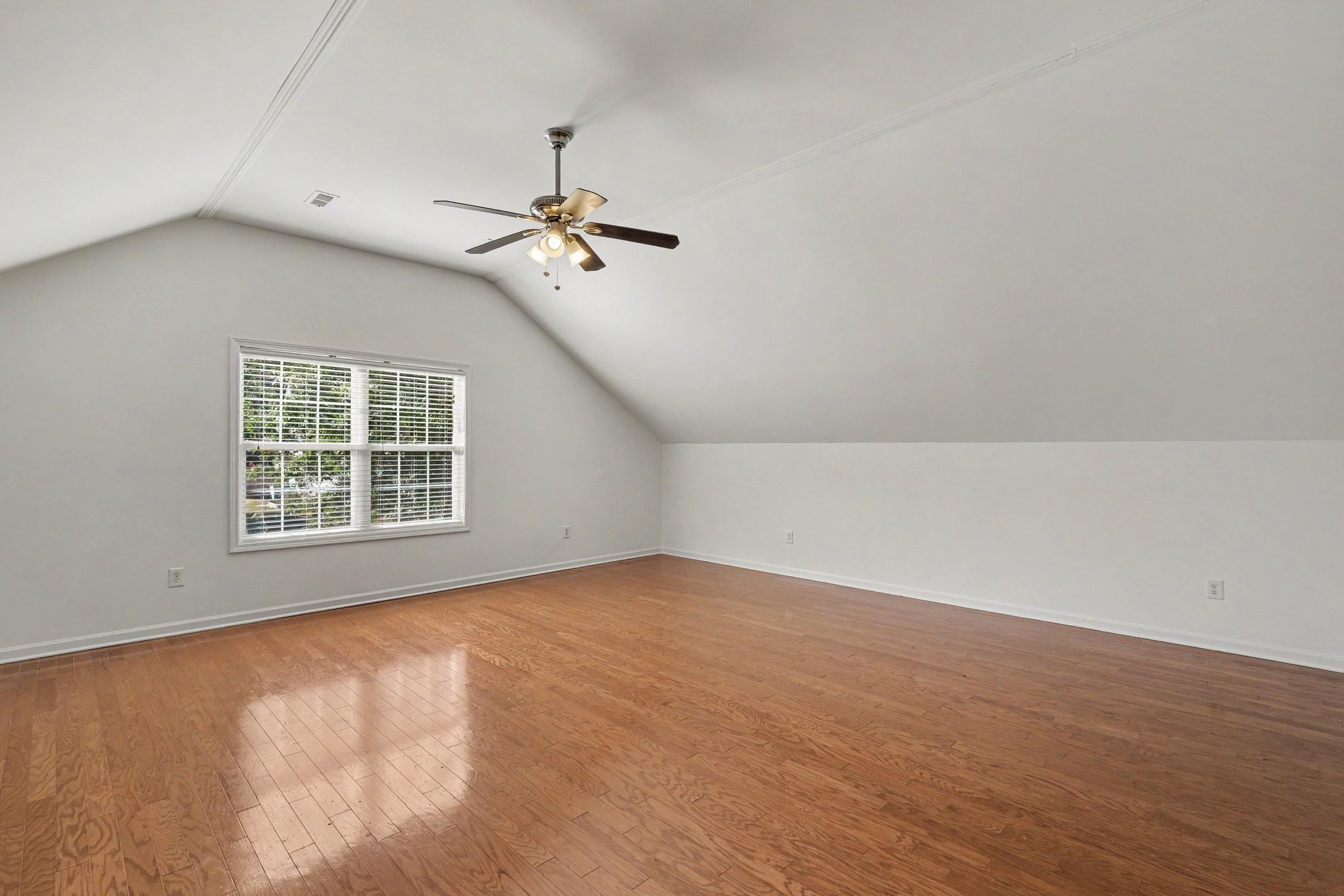 Empty room with hardwood floors, a sloped ceiling, ceiling fan, and window with blinds.