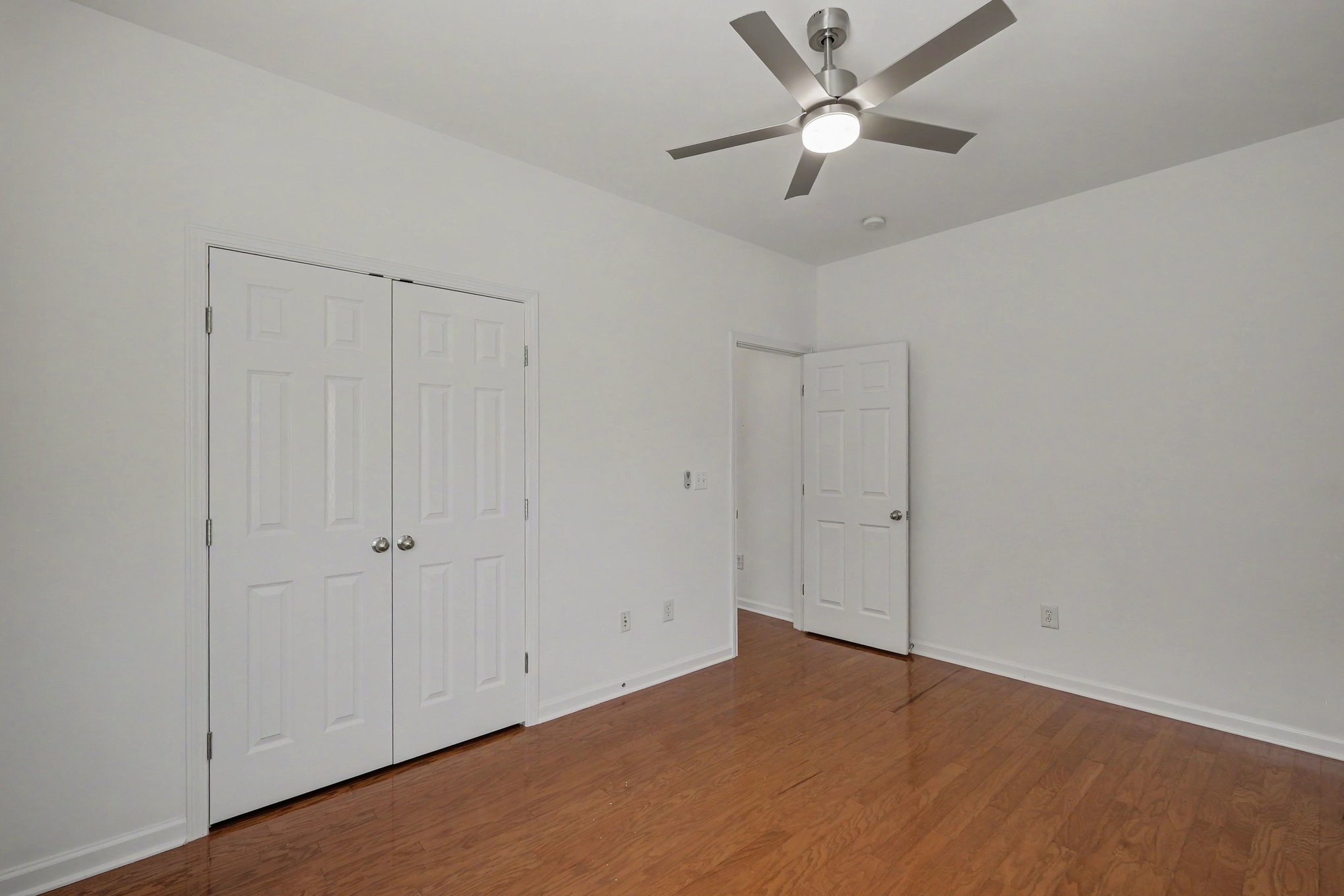 Empty bedroom with hardwood floors, double closet doors, and a ceiling fan.