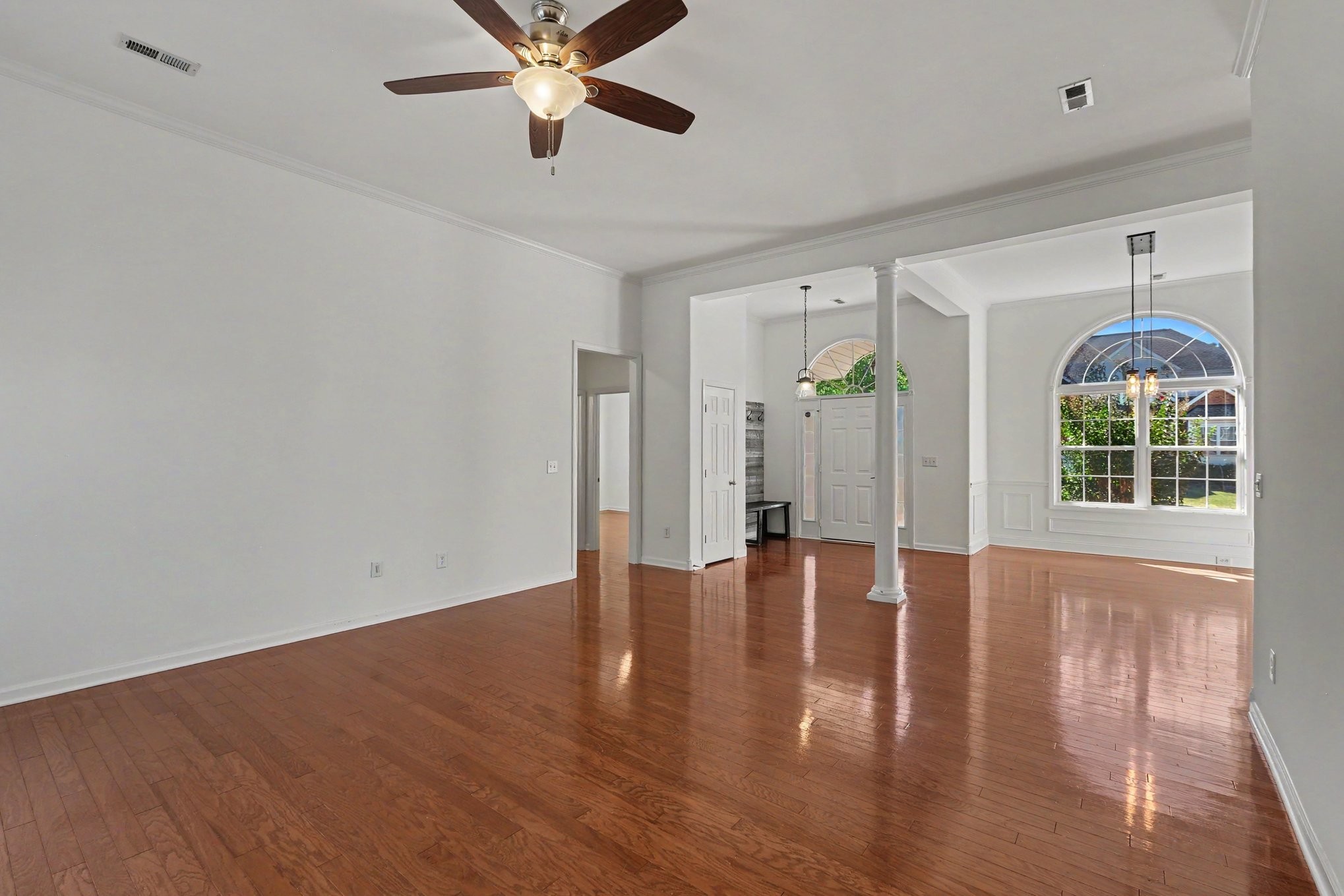 Vacant living room with hardwood floors, a ceiling fan, and a large arched window.
