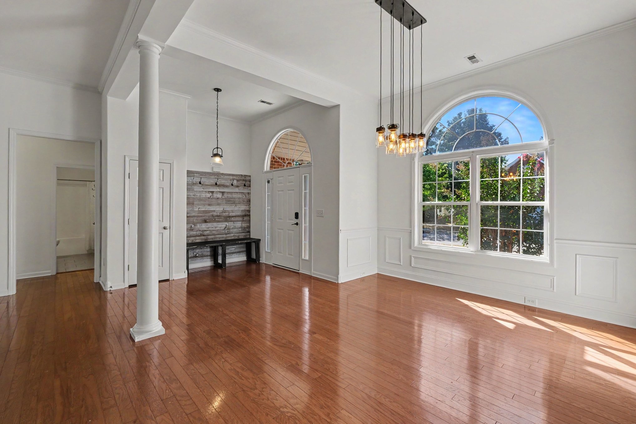 Vacant entryway with glossy hardwood floors, a large arched window, and a rustic bench by the front door.