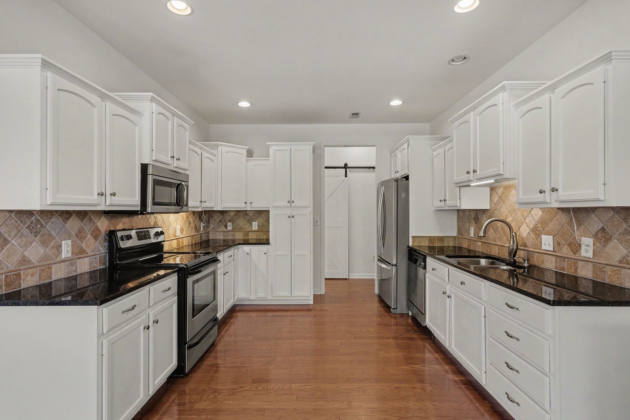 Kitchen with white cabinets, tan tile backsplash, dark countertops, stainless steel appliances, and wood flooring.