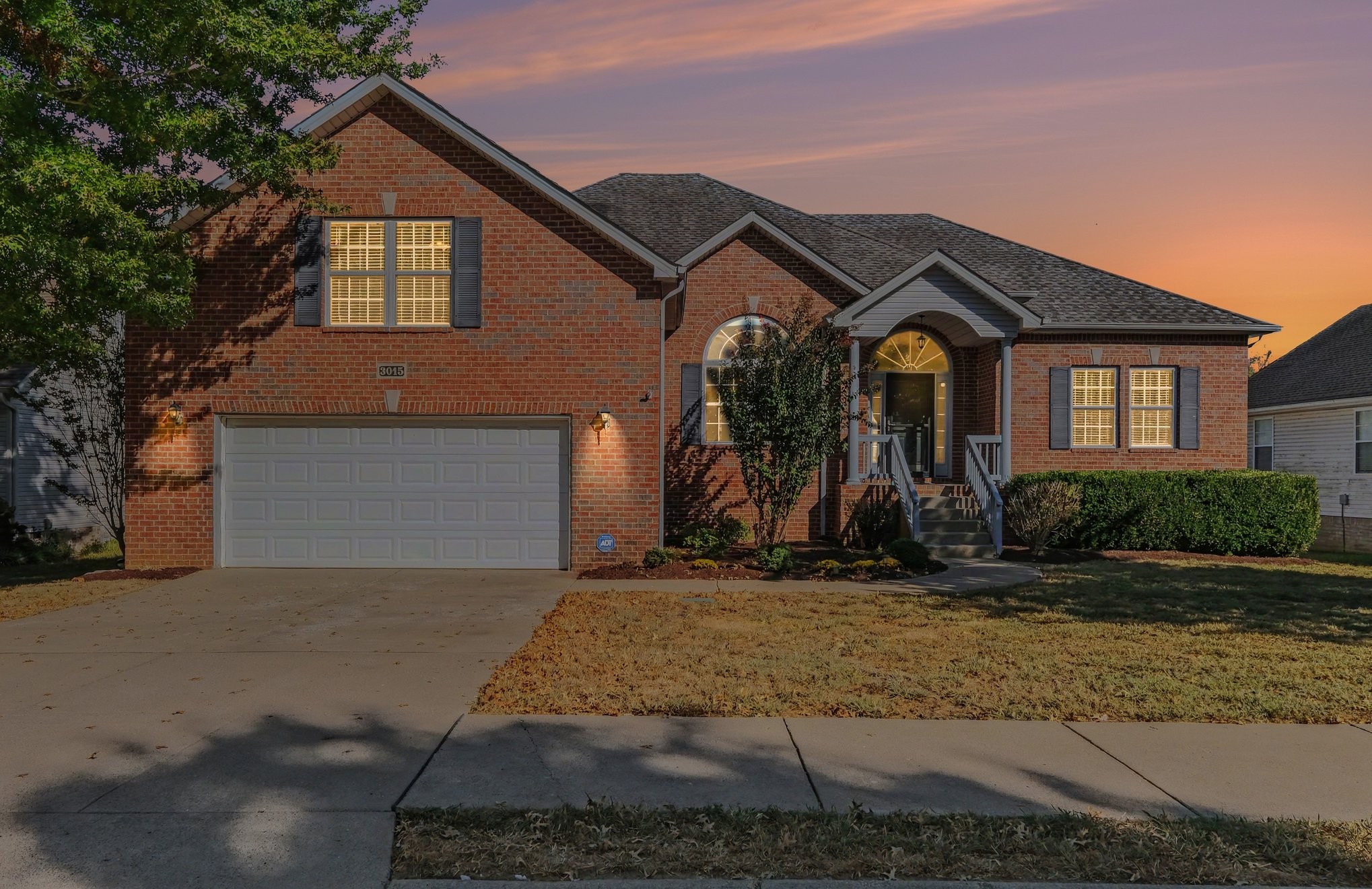 Brick home with a two-car garage and arched entryway beneath a pink-orange dusk sky.