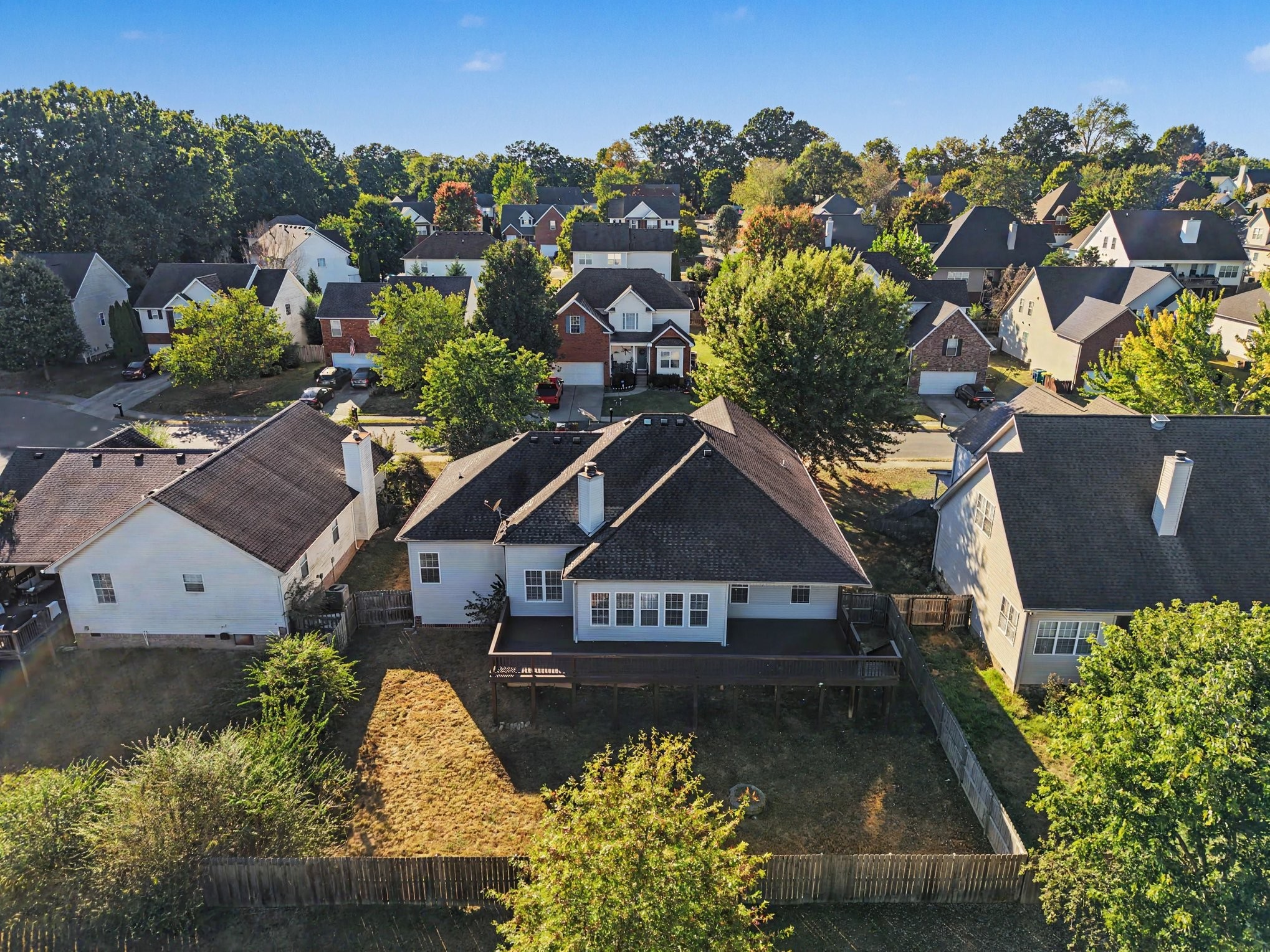 Aerial view of a suburban home with a raised deck, fenced backyard, and autumn trees.