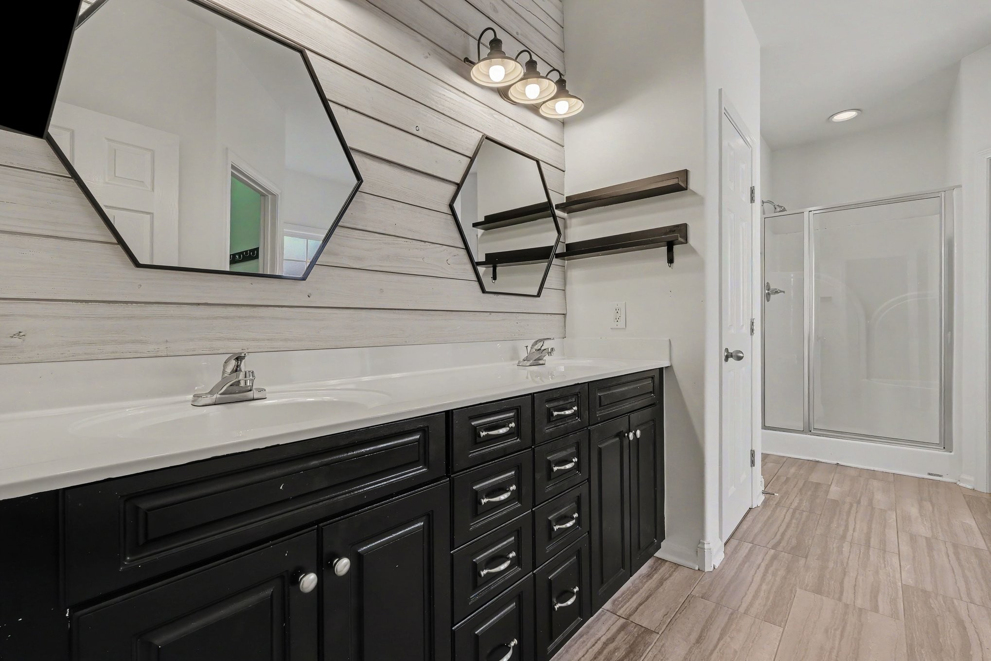 Bathroom with a double-sink vanity, black cabinetry, geometric mirrors, and a glass-enclosed shower.