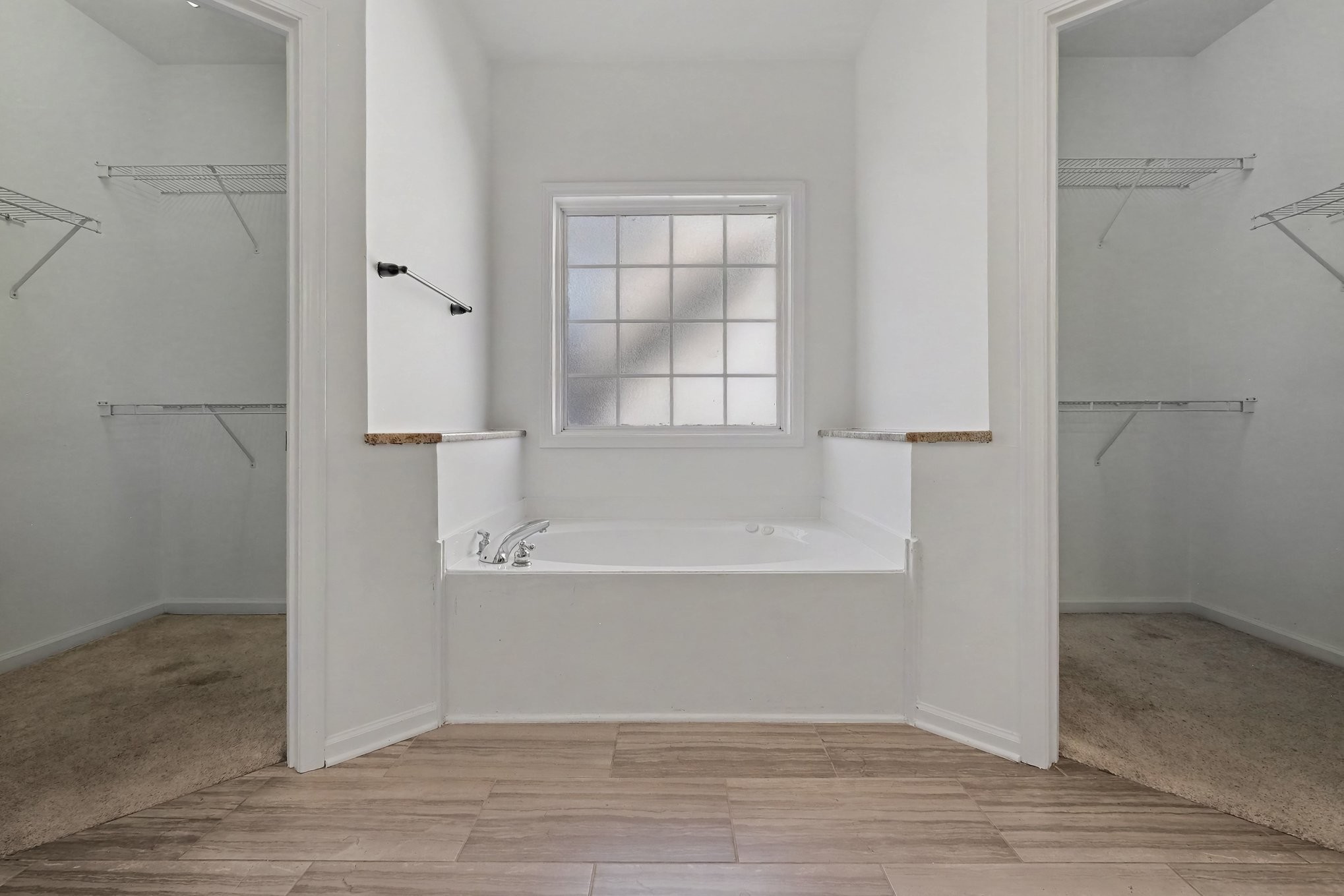 Built-in bathtub beneath a frosted window, between two open closets with wire shelves.