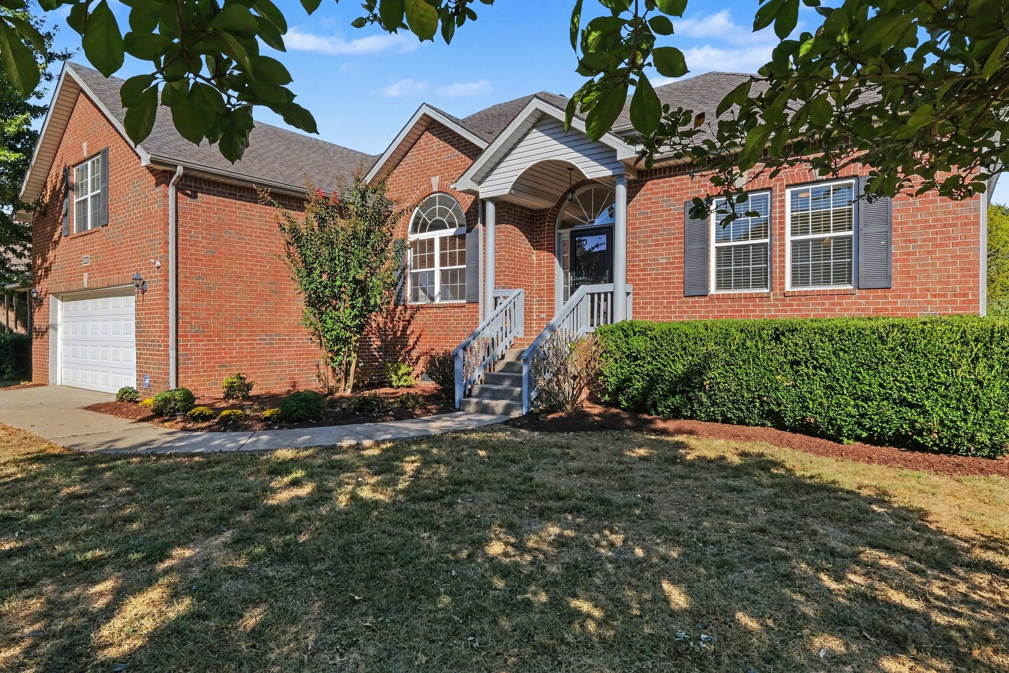Red brick house with a covered entry, white garage door, and trimmed hedges.