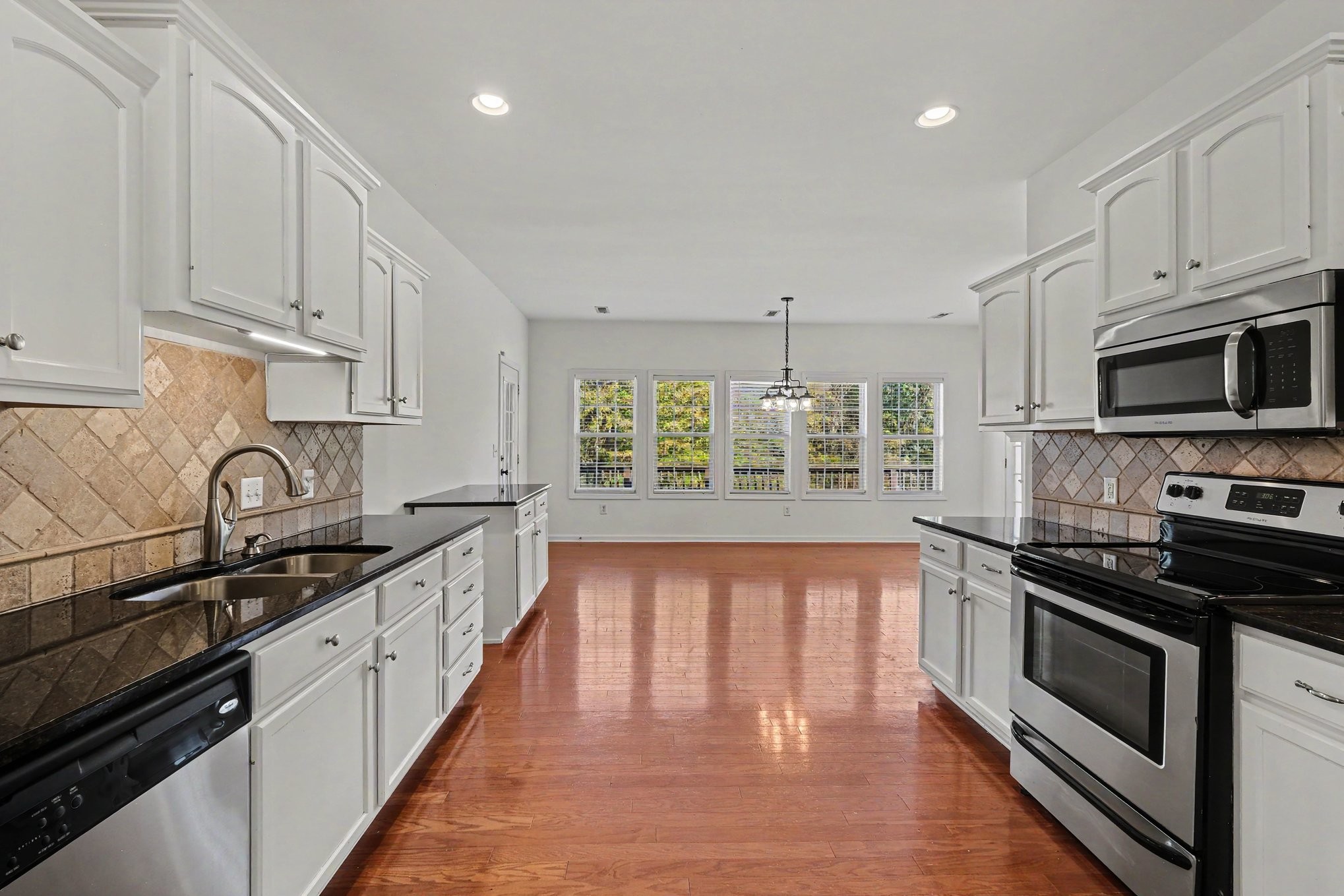 Kitchen with white cabinetry, dark counters, stainless appliances, and reddish hardwood floors.