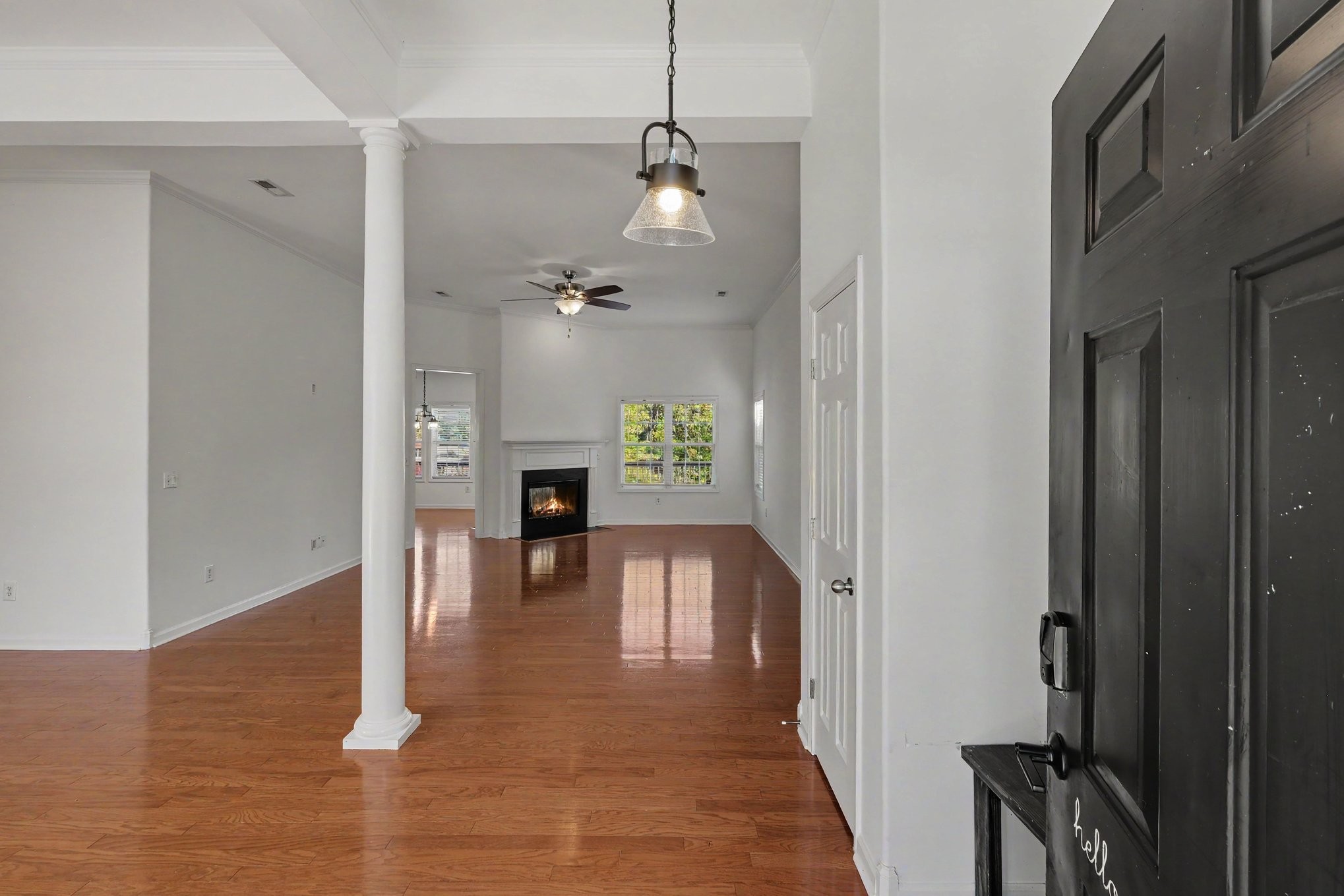 Empty living room with glossy hardwood floors, white columns, and a fireplace beneath a window.