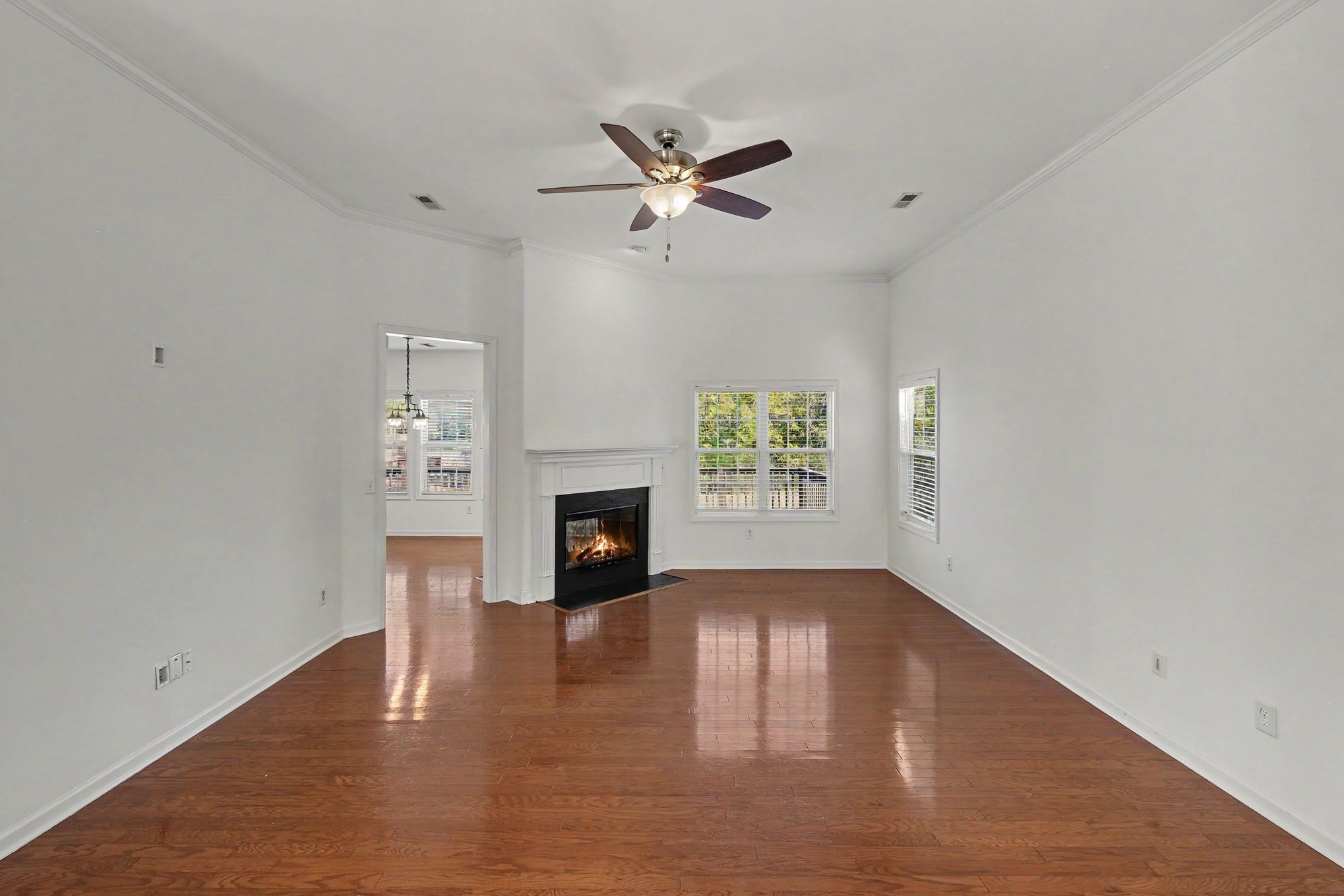 Empty living room with hardwood floors, a lit fireplace, and a ceiling fan.