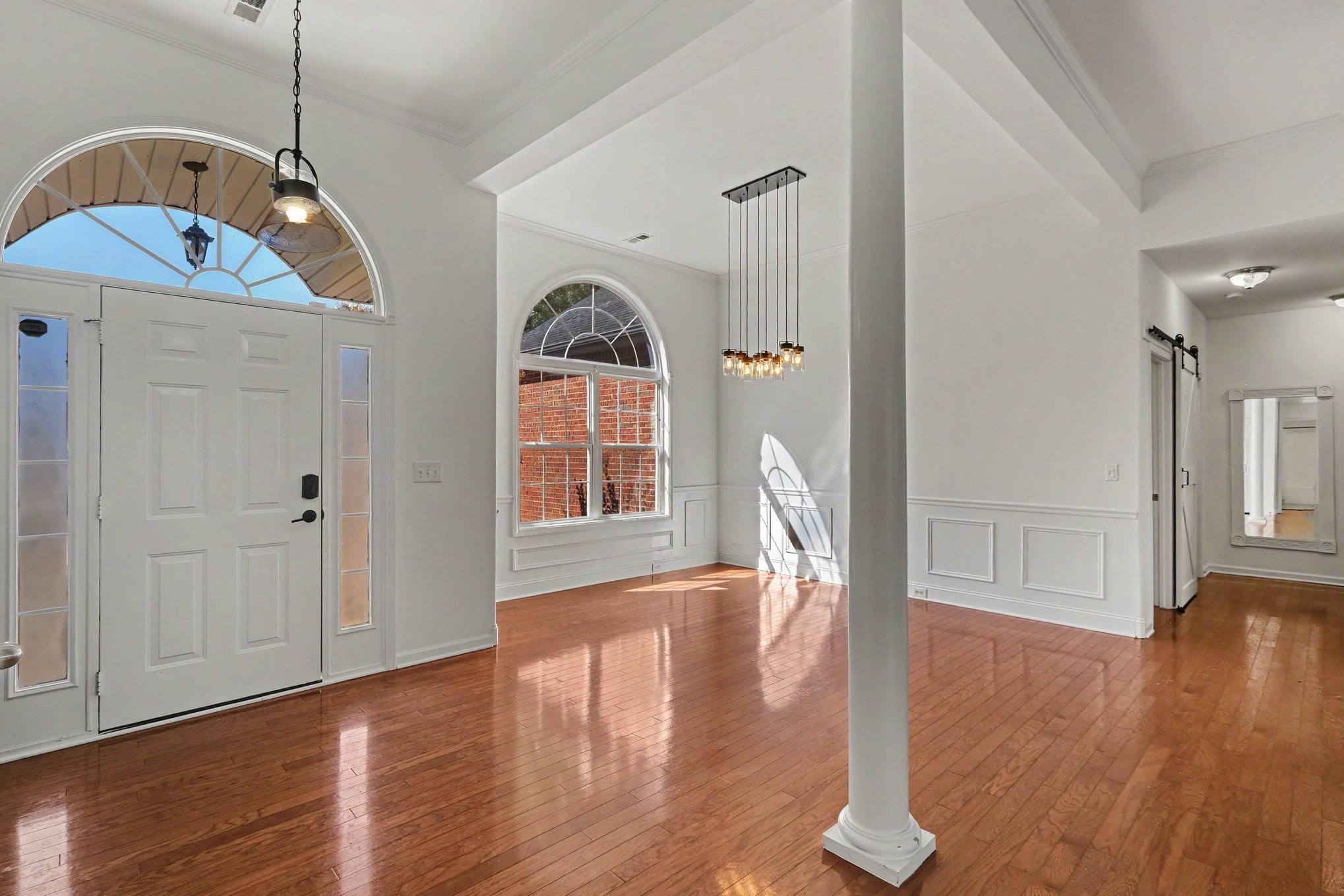 Vacant foyer with arched windows, polished hardwood floors, and a tall white column.