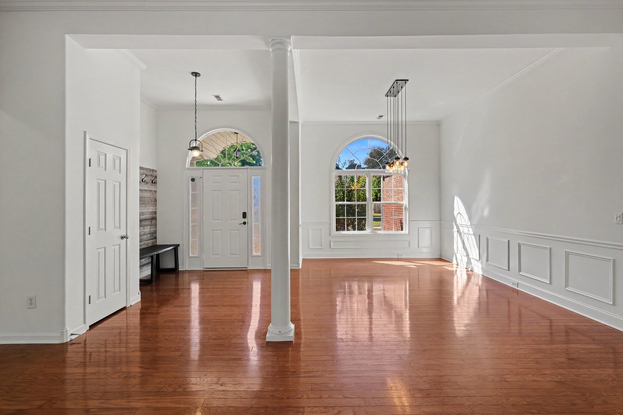 Vacant entry hall with polished hardwood floors, a central column, and arched windows beside the front door.