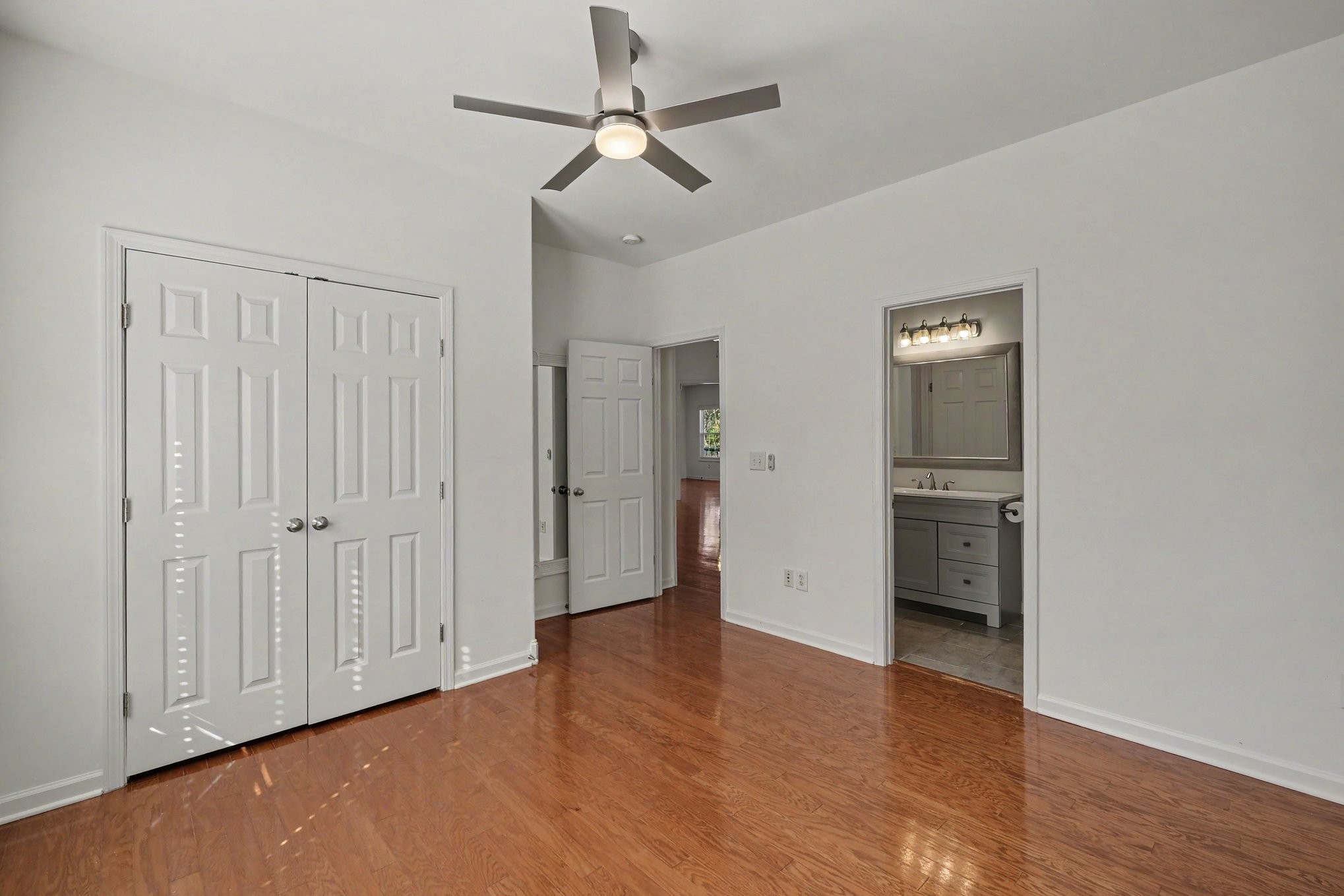 Unfurnished bedroom with hardwood floors, double closets, a ceiling fan, and an adjoining bathroom.