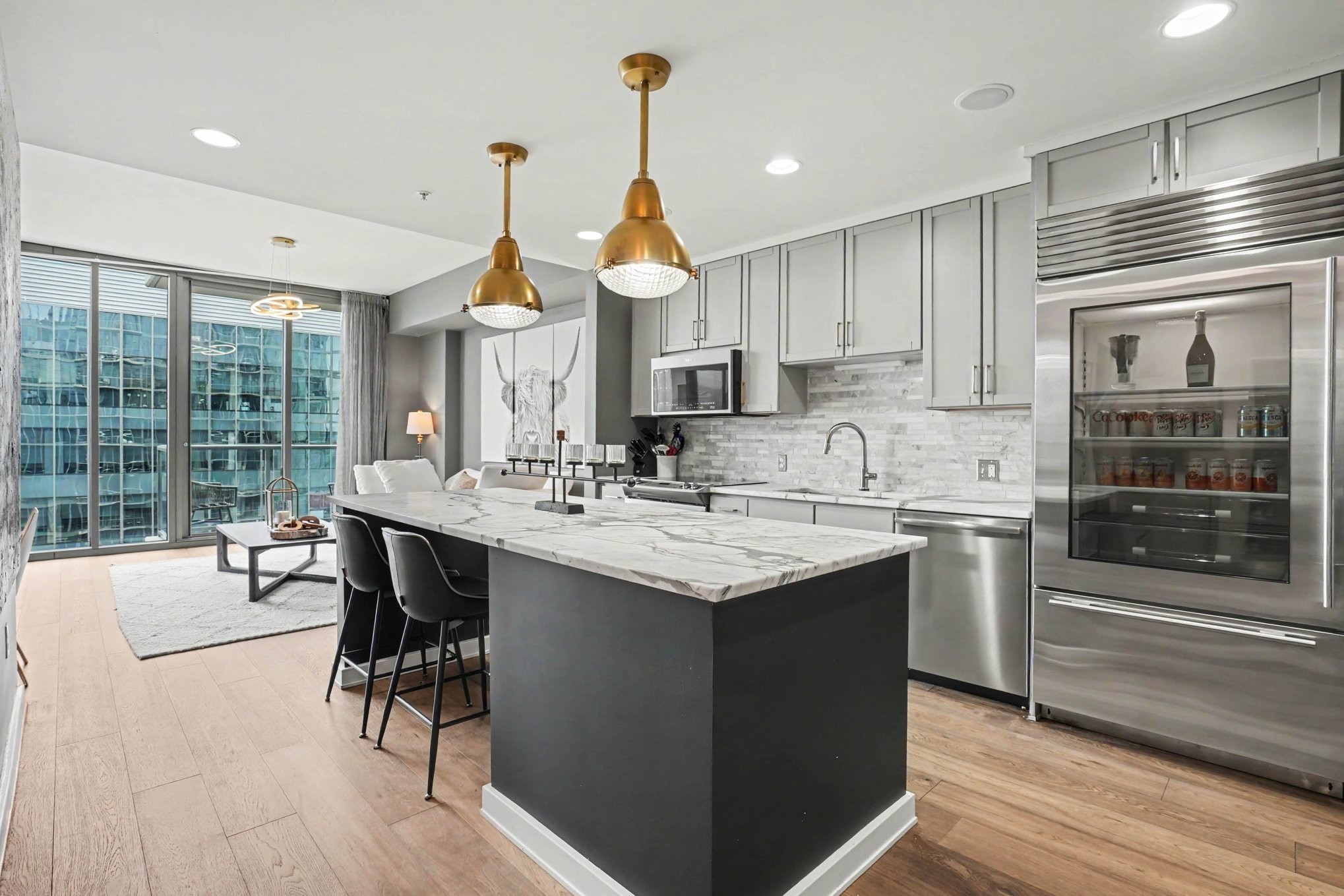 Modern condo kitchen with a large marble island, brass pendants, stainless appliances, and city views.