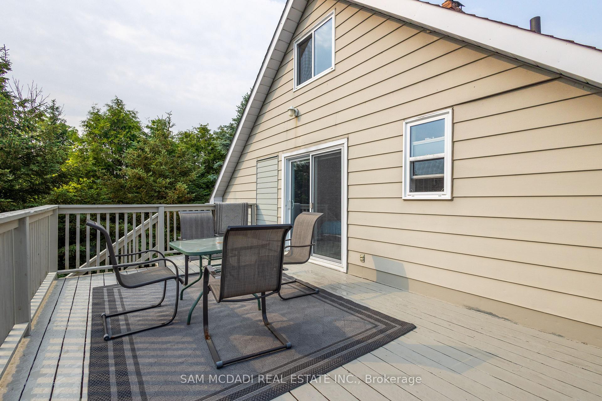 Furnished wooden deck beside a beige house, with patio chairs and a table near sliding glass doors.