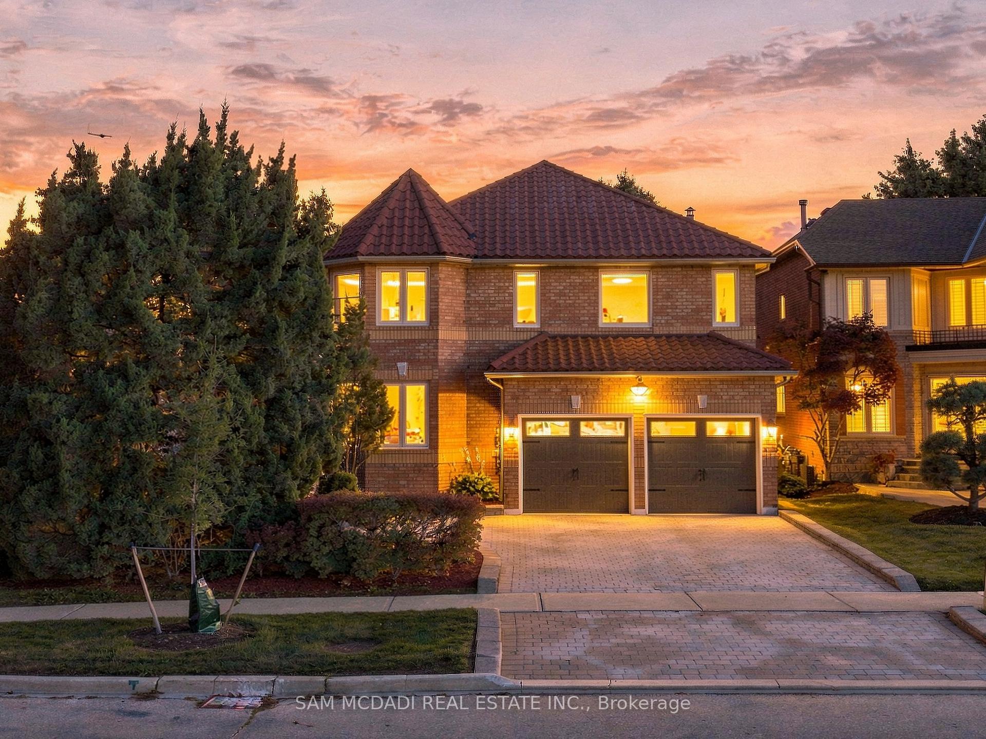 Two-story brick house with a double garage and illuminated windows at dusk.