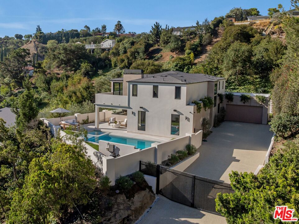 Modern hillside home with a turquoise pool, patio, and gated driveway.