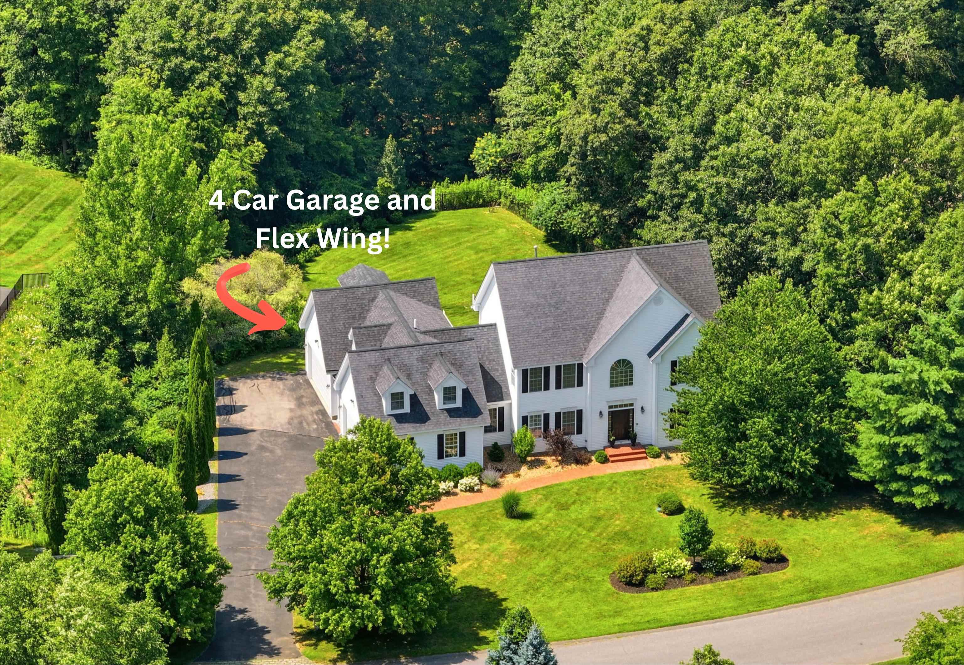 Aerial view of a white multi-wing home with a four-car garage, broad lawn, and surrounding trees.
