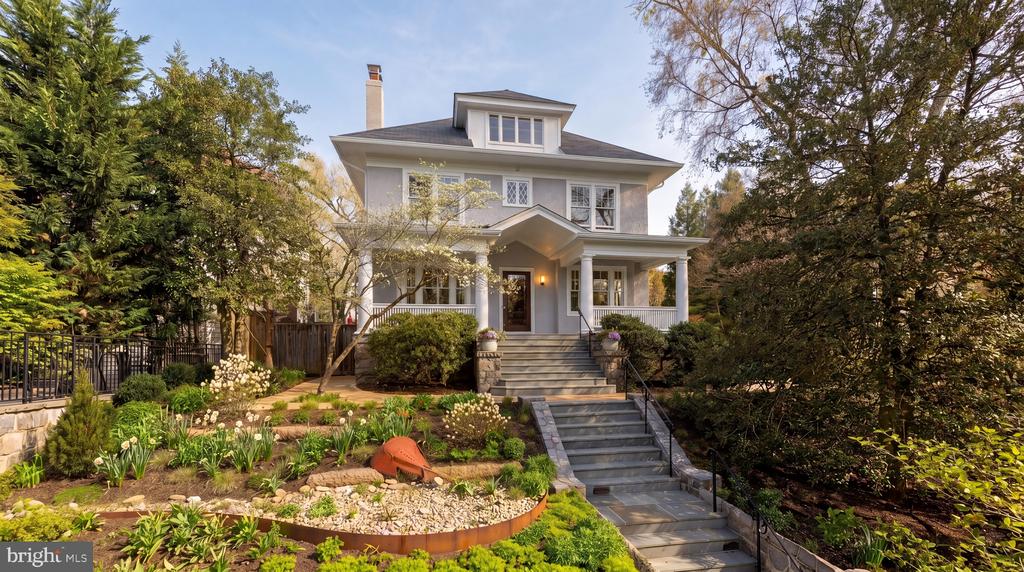 Gray two-story house with a covered porch, broad stone steps, and landscaped front garden.