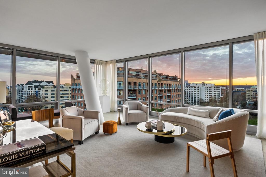 Living room with curved cream sofas and corner windows overlooking downtown at sunset.