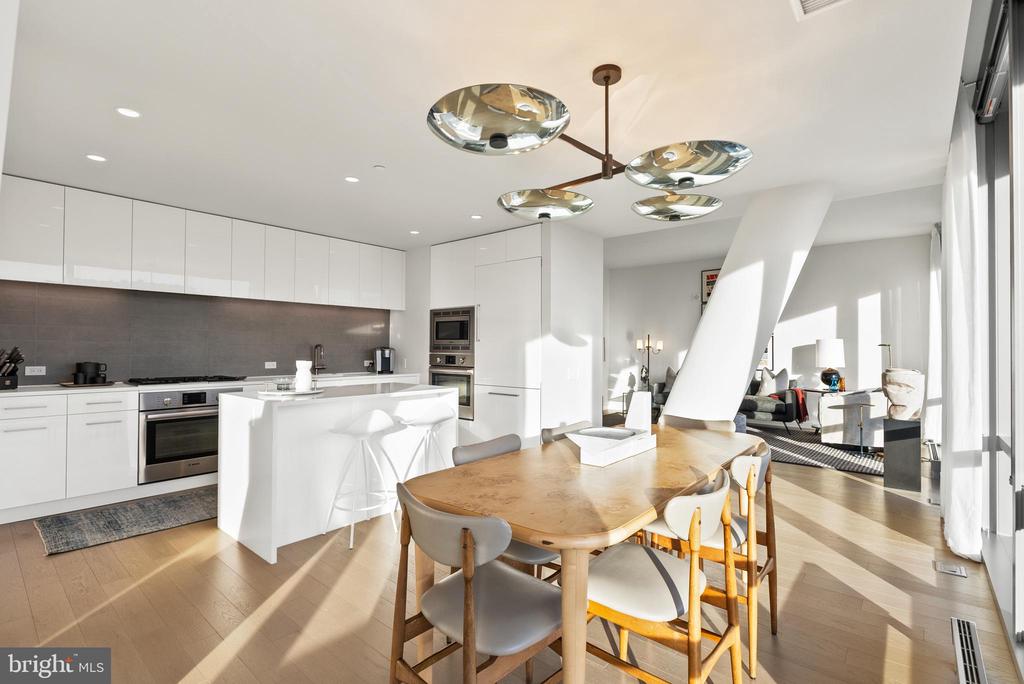 Open-plan kitchen and dining area with a white island, wooden table, and sunlit windows.