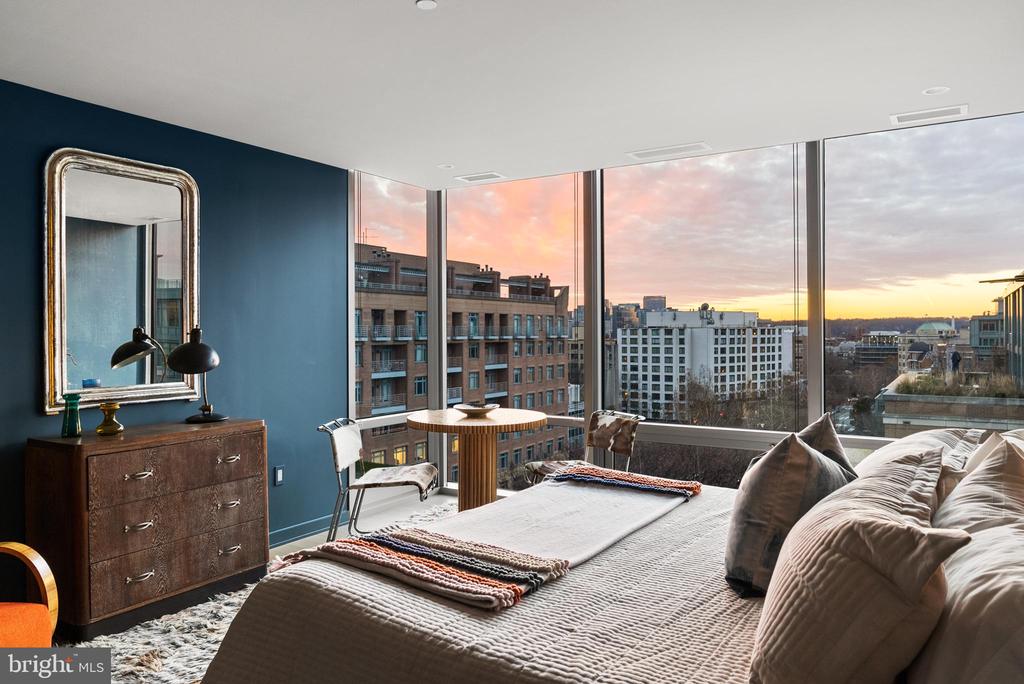 Bedroom with floor-to-ceiling windows overlooking the city at sunset.
