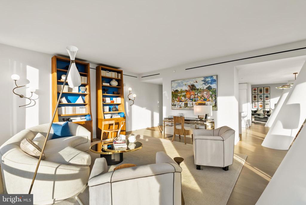 Sunlit living room with curved seating, tall wooden bookshelves, and colorful artwork.