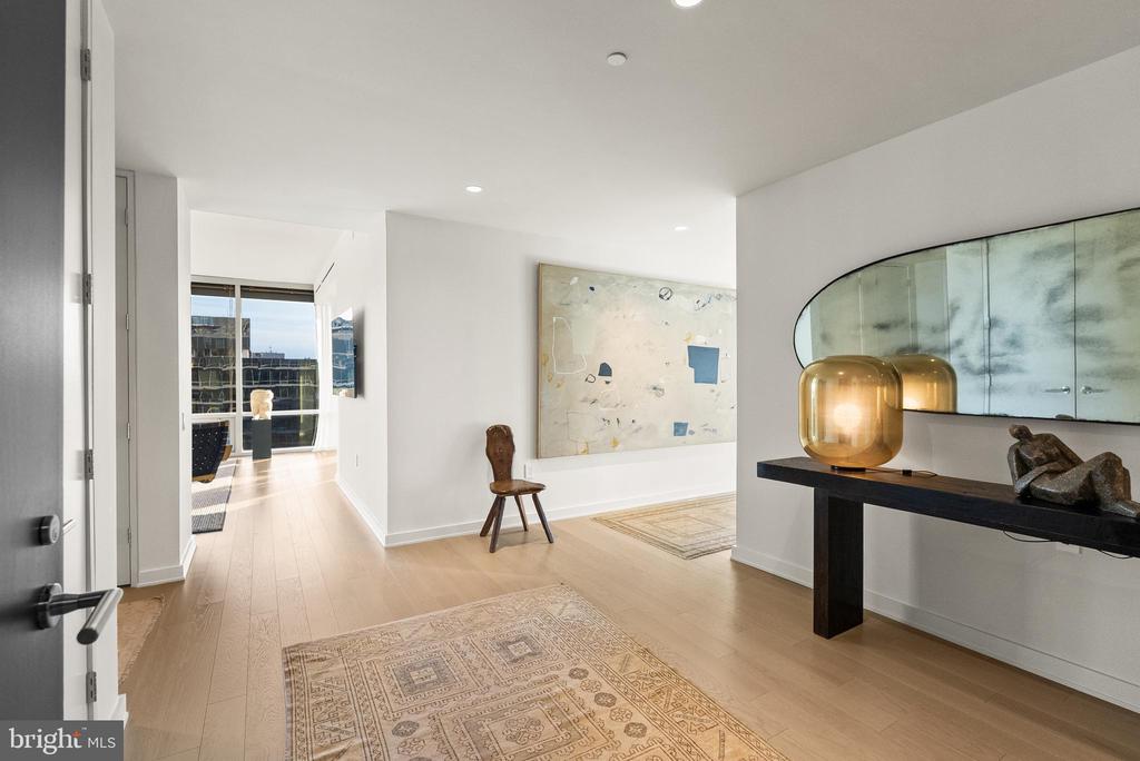 Modern condo entry hall with light wood floors, abstract artwork, and a black console table with amber lamps.