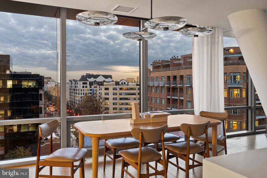 Dining area with a wooden table and chairs overlooking the city through floor-to-ceiling windows.