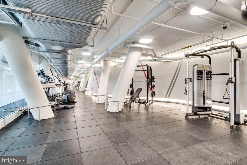 Fitness room with weight machines, cardio equipment, tiled floors, and large windows.