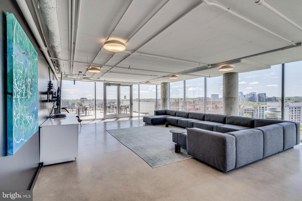 Modern furnished living room with gray sectional, floor-to-ceiling windows, and Washington, D.C. city views.