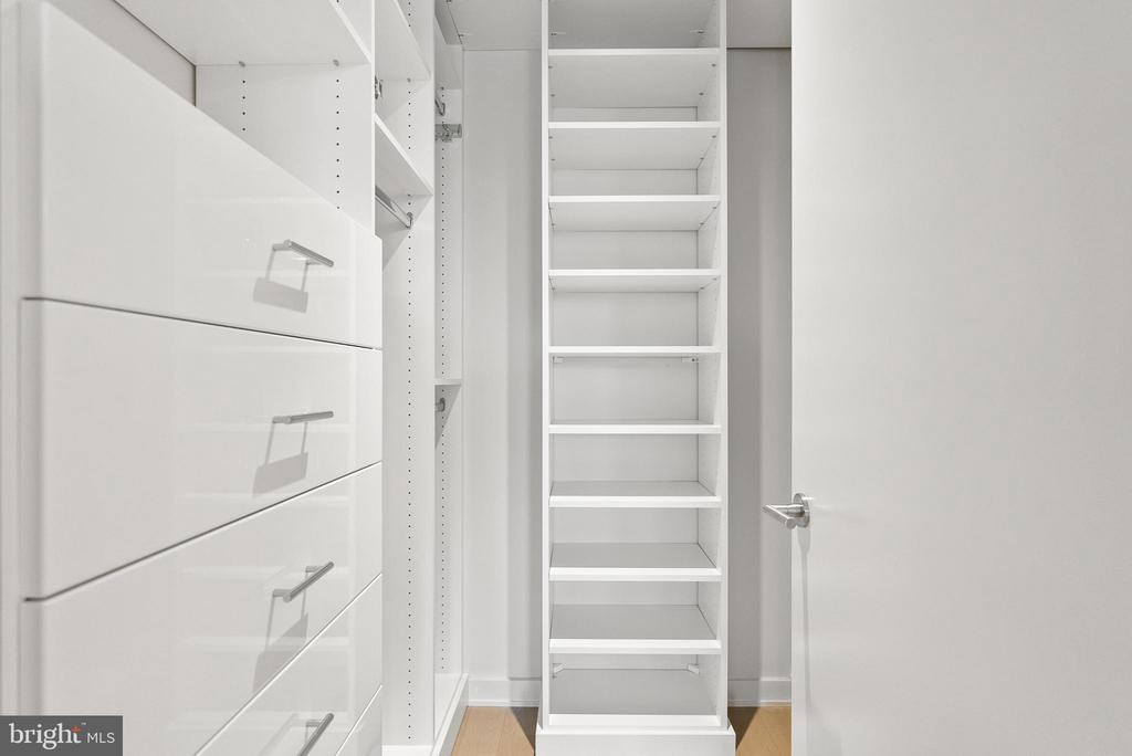 Walk-in closet with white built-in drawers and shelves and light wood flooring.