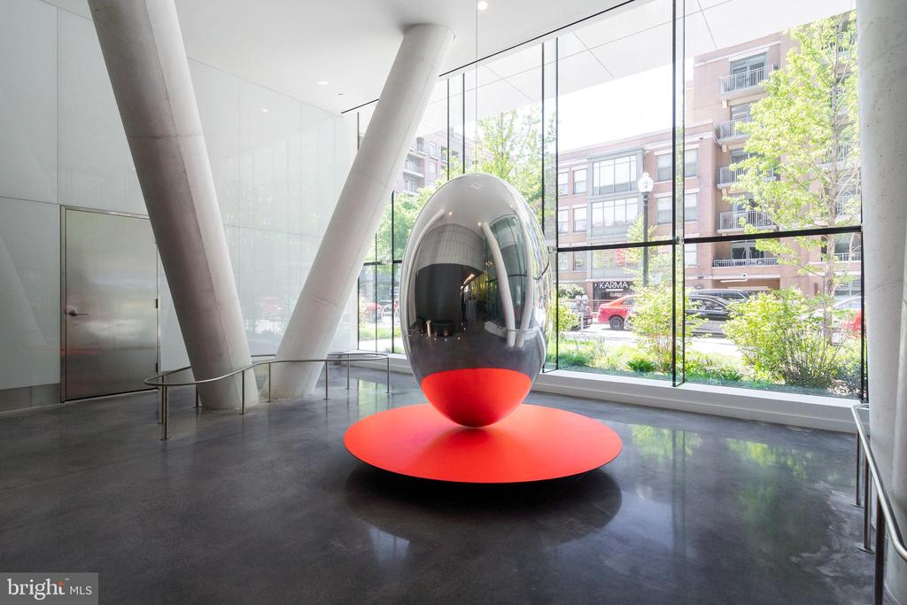 Modern lobby with angled concrete columns and a reflective sculpture on a bright red circular base.