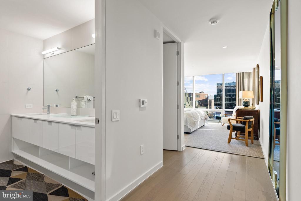 Modern bathroom vanity opens onto a furnished bedroom with large windows.