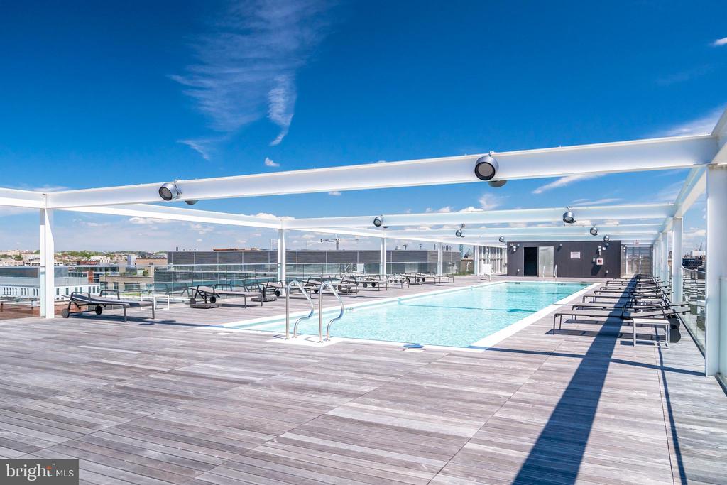 Rooftop pool with lounge chairs on a spacious deck beneath a white canopy.