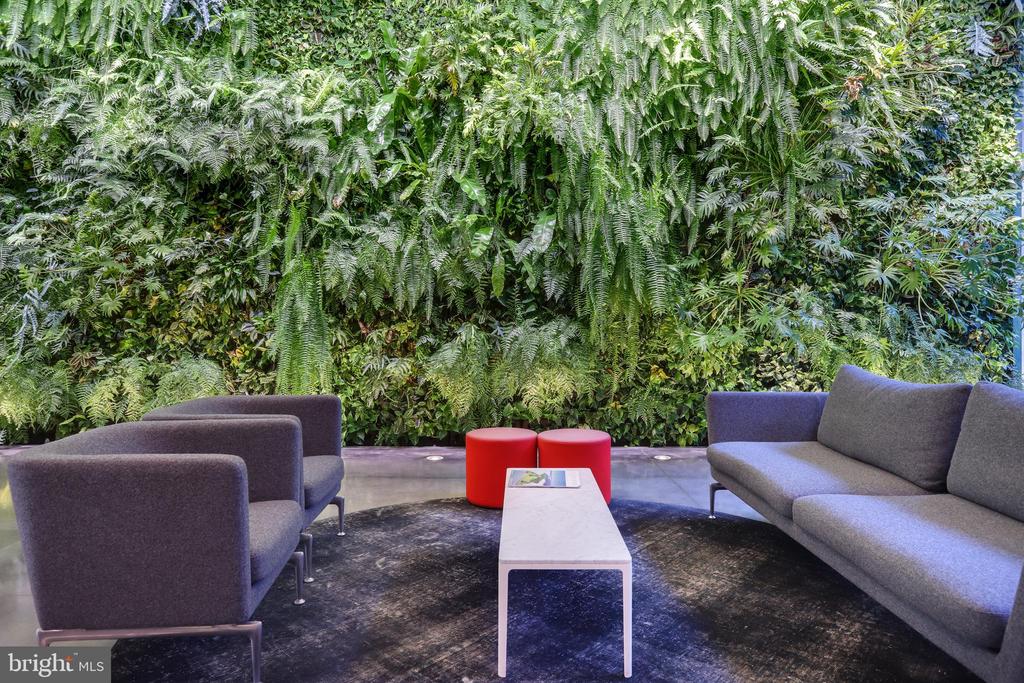 Furnished lounge with gray seating, red stools, and a lush floor-to-ceiling fern wall.