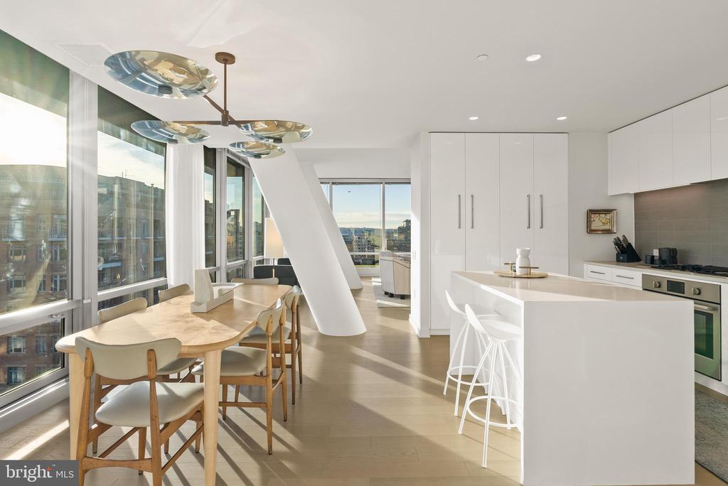 Modern condo kitchen and dining area with a large island and floor-to-ceiling city-facing windows.