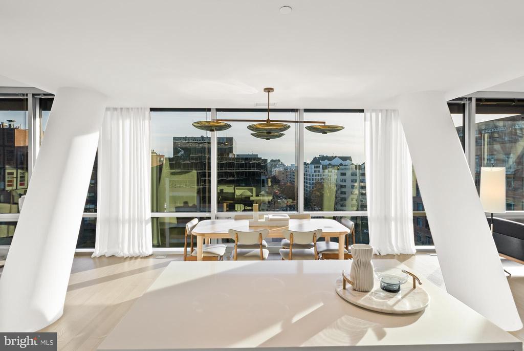 Modern dining area with a brass chandelier and city views through floor-to-ceiling windows.