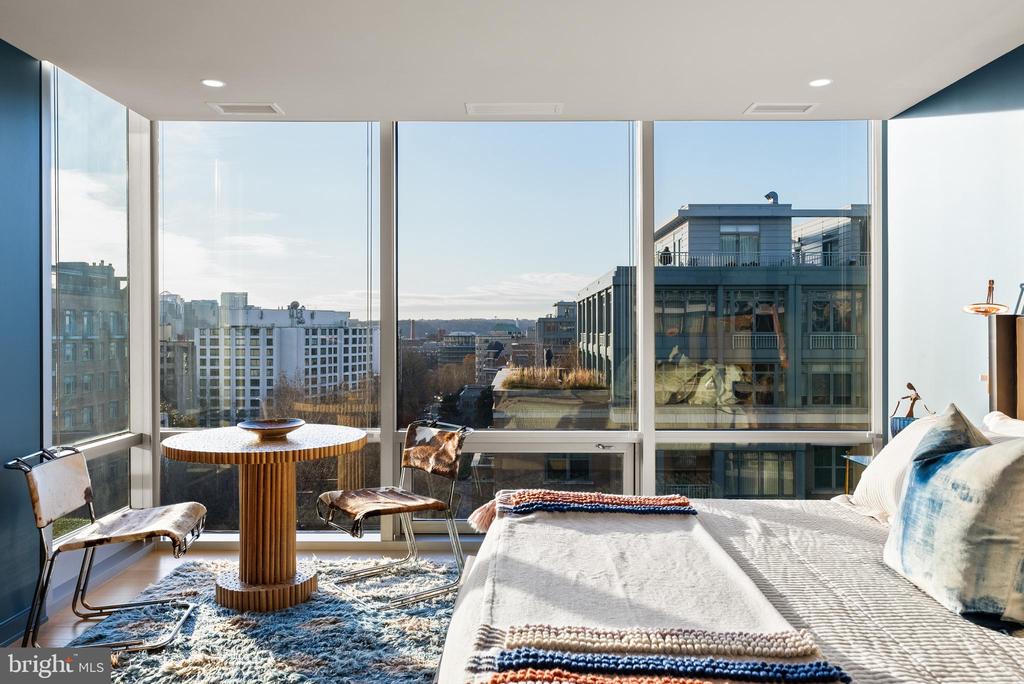 Bedroom with floor-to-ceiling windows, city views, and a round table with two chairs.
