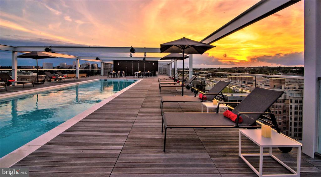 Rooftop pool and lounge deck at sunset, with city buildings in the distance.