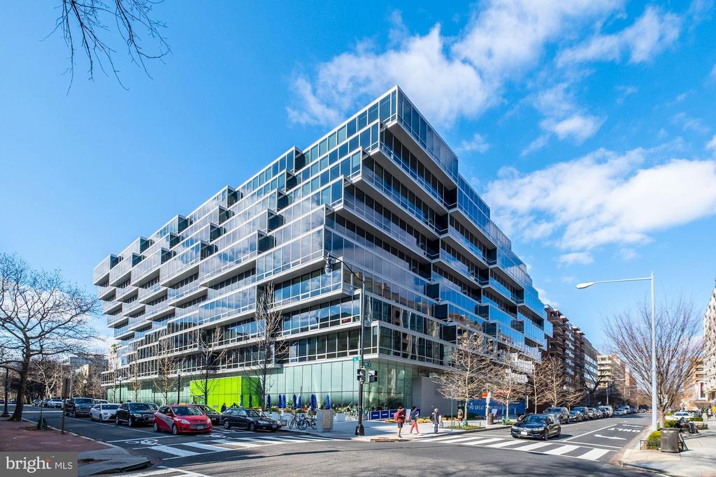 Modern glass condominium building on a Washington, D.C. street corner, with stacked balconies.