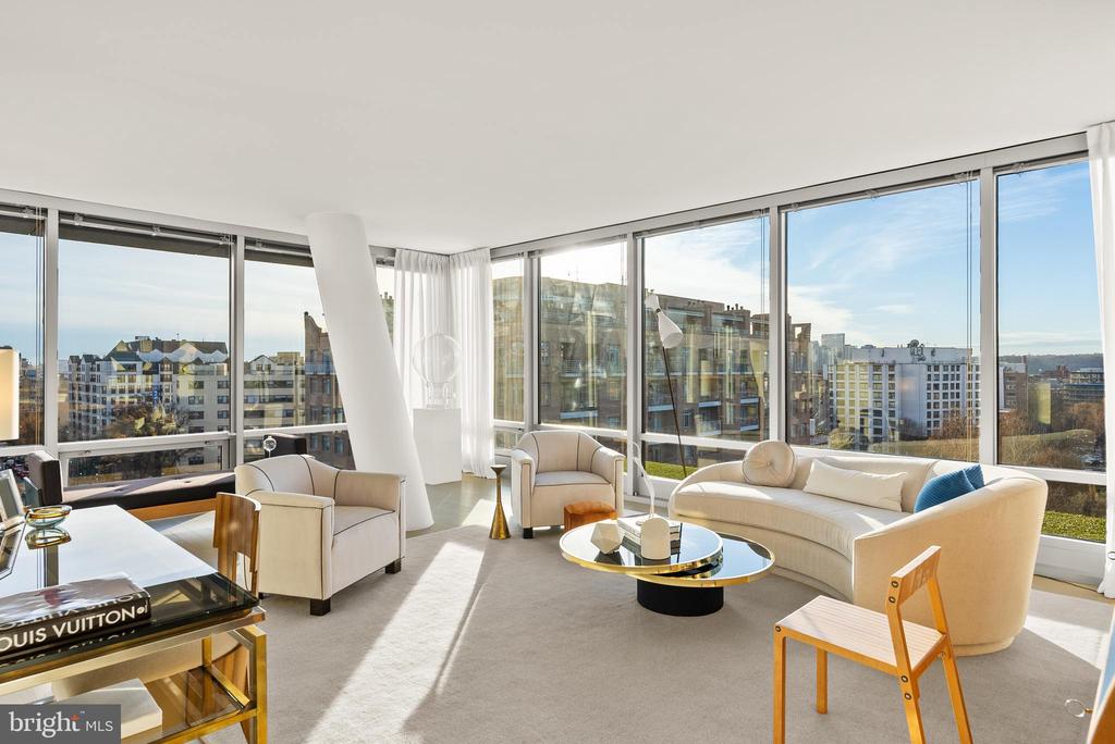 Furnished condo living room with floor-to-ceiling windows overlooking Washington, DC buildings.