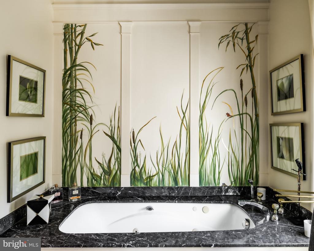Bathroom soaking tub framed by black marble, with a tall grass mural behind it.